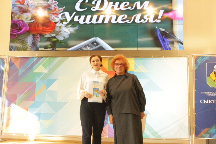 На фотографии учительница держит грамоту, а рядом с ней стоит директор гимназии..