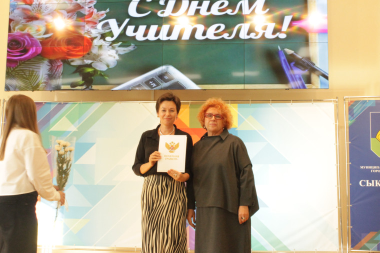 На фотографии учительница держит грамоту, а рядом с ней стоит директор гимназии..